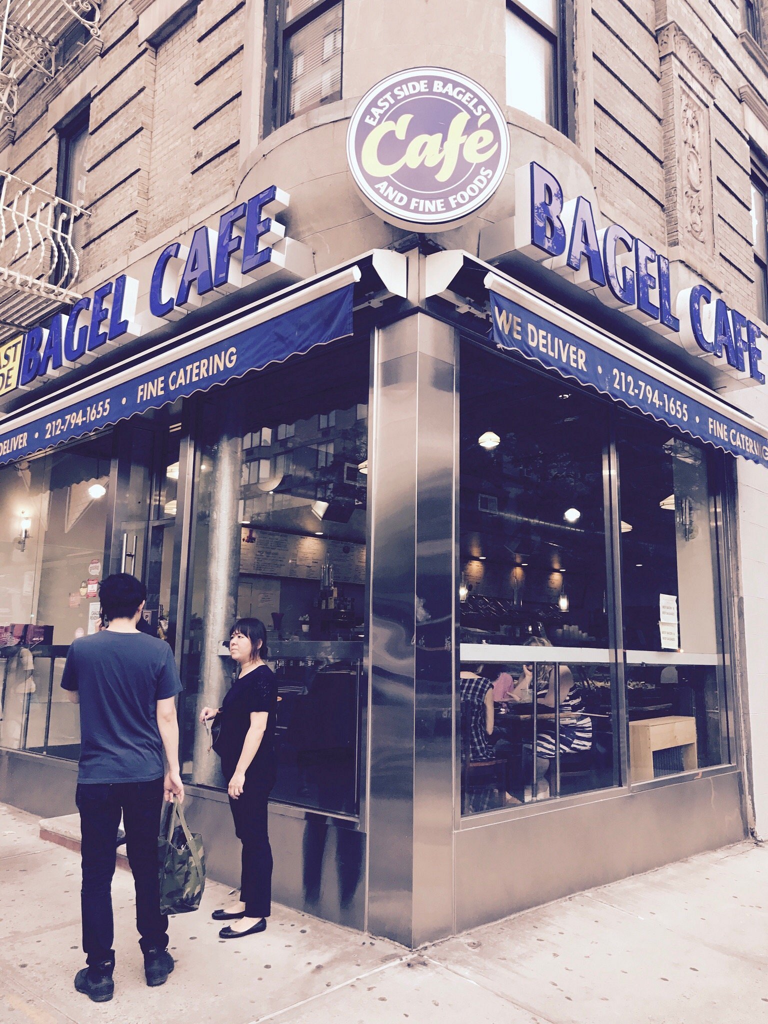 The East Side Bagel Cafe storefront: the round Cafe sign above blue Bagel Cafe awnings on the corner